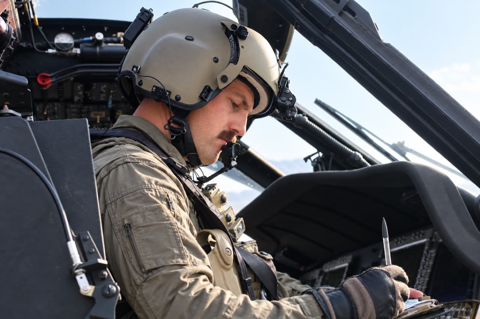 Ein Pilot mit Helm prüft im Cockpit eines Hubschraubers seine Instrumente.